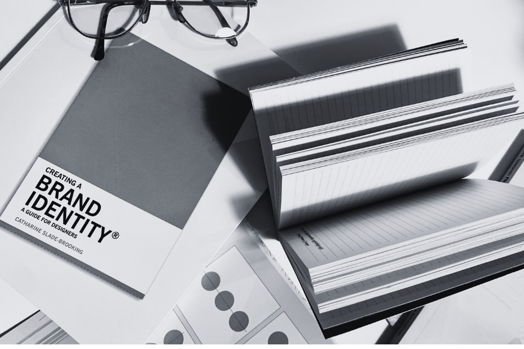 Visual identity design elements including a brand identity book, color samples, and notebooks on a desk.